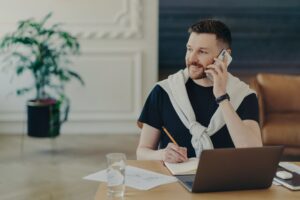 Pleasant freelancer talking on mobile phone while working from home
